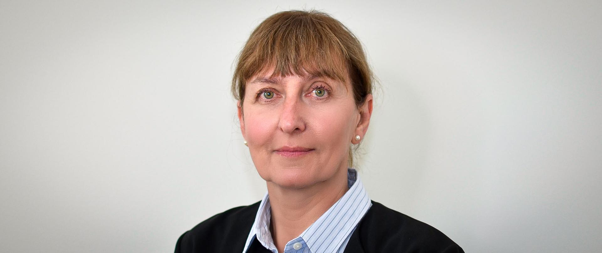 Kobieta w czarnym żakiecie, błękitnej bluzce w cienkie paski, z grzywką i włosami średni brąz.