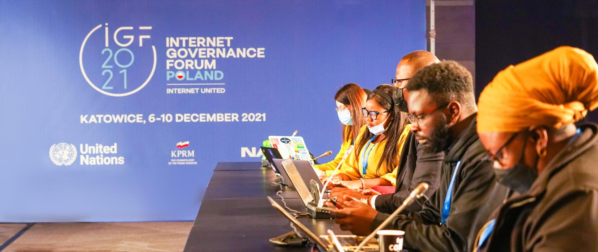 Uczestnicy panelu IGF Afryka, siedzą po prawej stronie za stołem. Za nimi, na całek szerokości, ścianka z logo IGF 2021.