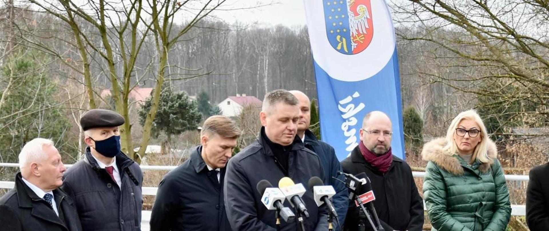 Na zdjęciu znajduje się osiem osób, stoją na drodze