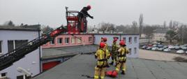 Zdjęcie wykonane w ciągu dnia. Ratownicy ubrani w ubrania specjalne. Wykonują czynności związane z ratownictwem wysokościowym