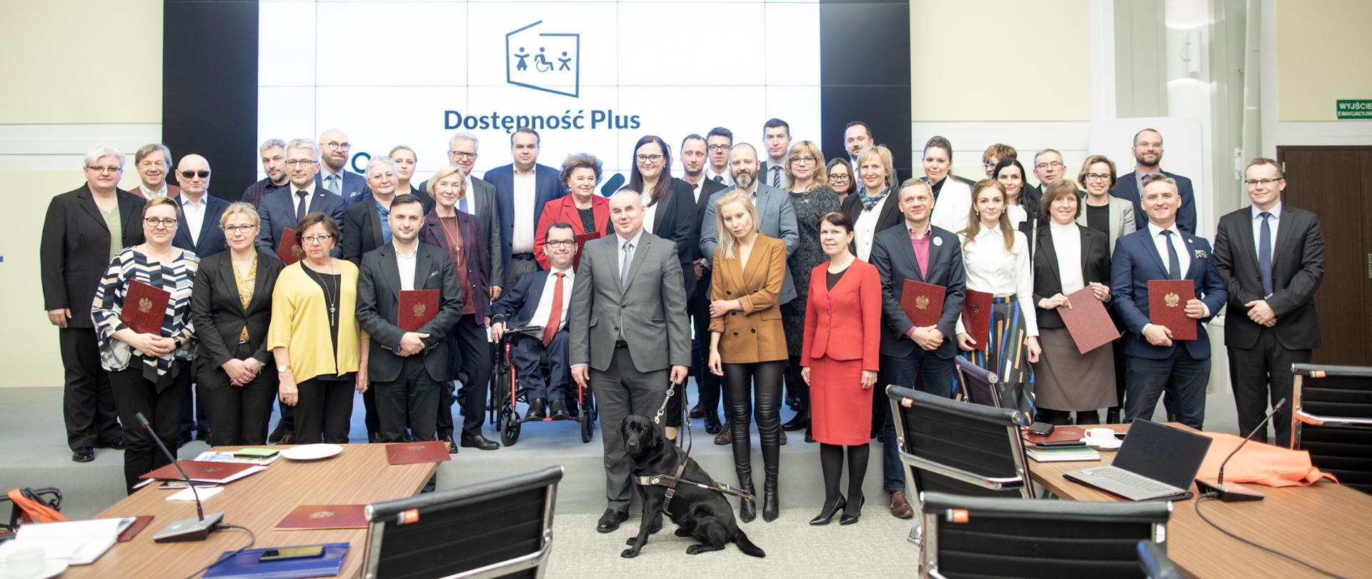 członkowie Rady Dostępności pozują do grupowego zdjęcia za nimi napis Dostępność Plus