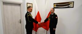 Zastępca pomorskiego komendanta wojewódzkiego Państwowej Straży Pożarnej wręcza czerwoną teczkę strażakowi.
