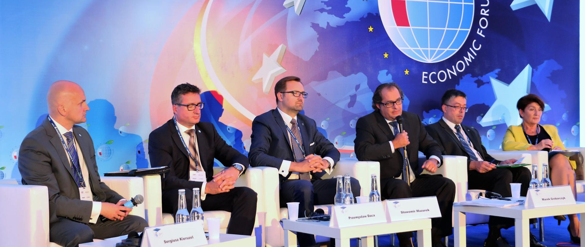 Minister Marek Gróbarczyk przemawia na jednym z paneli dyskusyjnych podczas Forum. Obok niech siedzi sześciu panelistów.