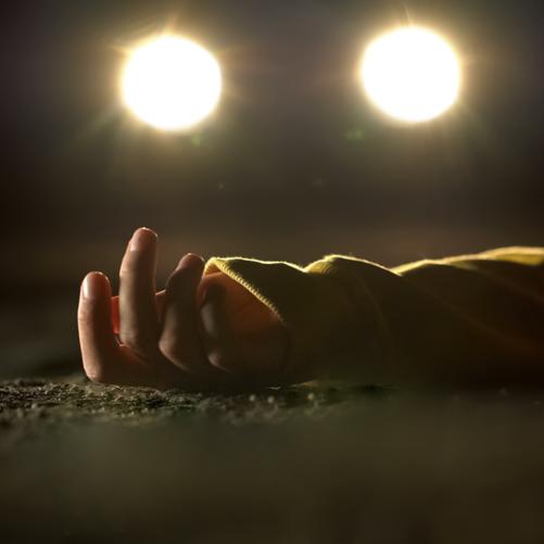 W ciemności widać światła samochodu, w których świetle widać leżącą na ziemi rękę dziecka.