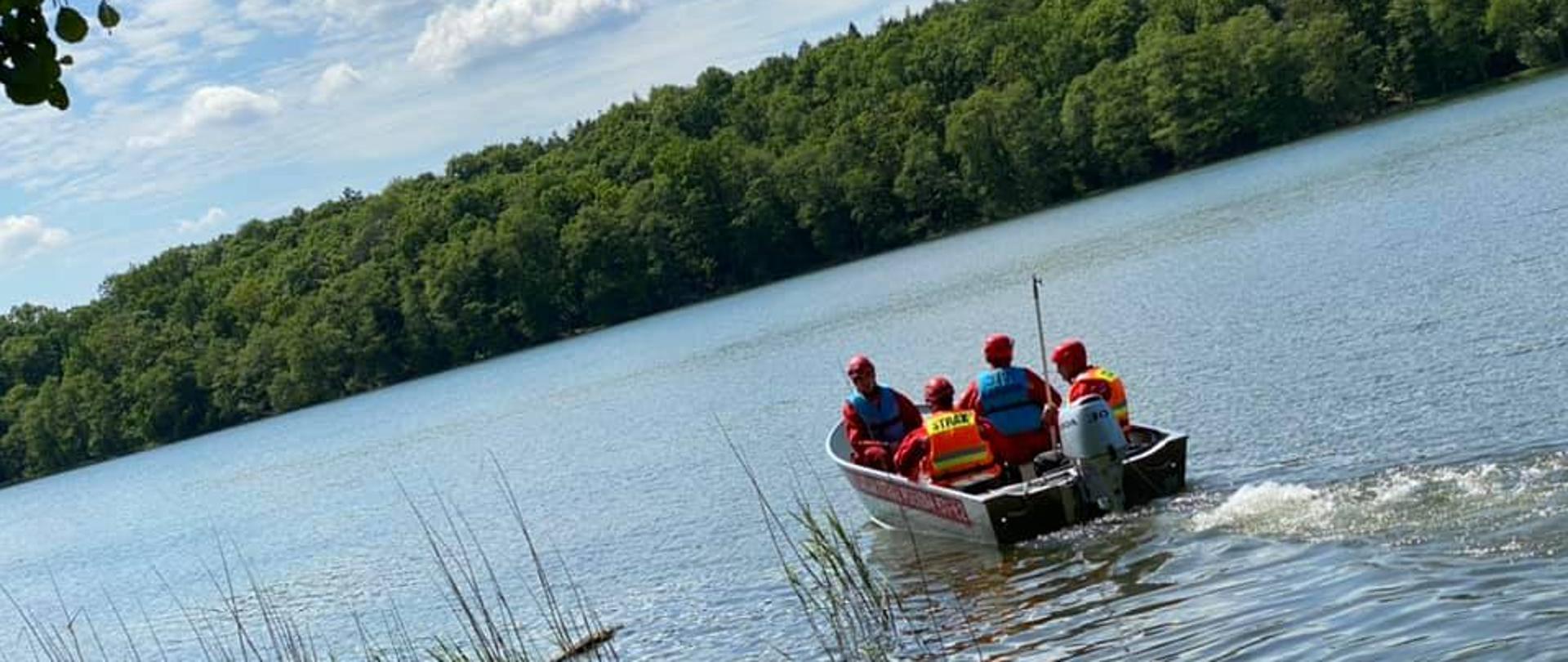 Zdjęcie przedstawia płynącą łódź silnikową z czterema ratownikami ubranymi w ubrania do pracy w wodzie.