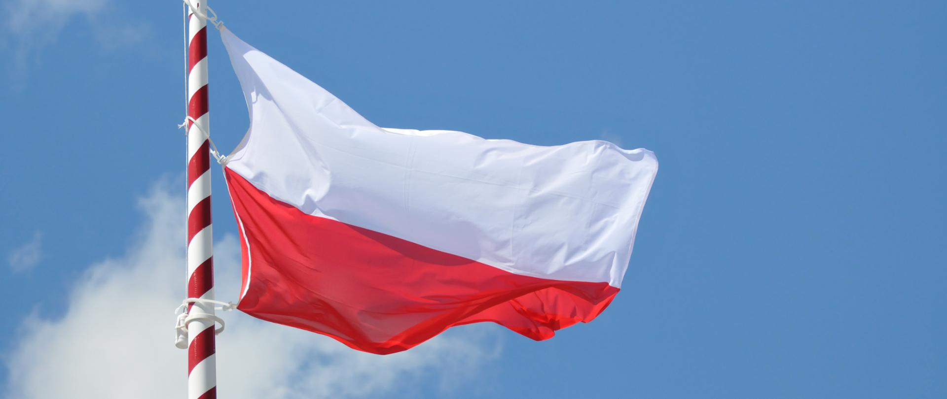Biało czerwona flaga powiewa na tle błękitnego nieba