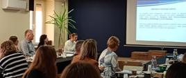 Uczestnicy szkolenia siedzą w sali konferencyjnej patrzą na ekran w głębi sali, na którym wyświetlona jest prezentacja