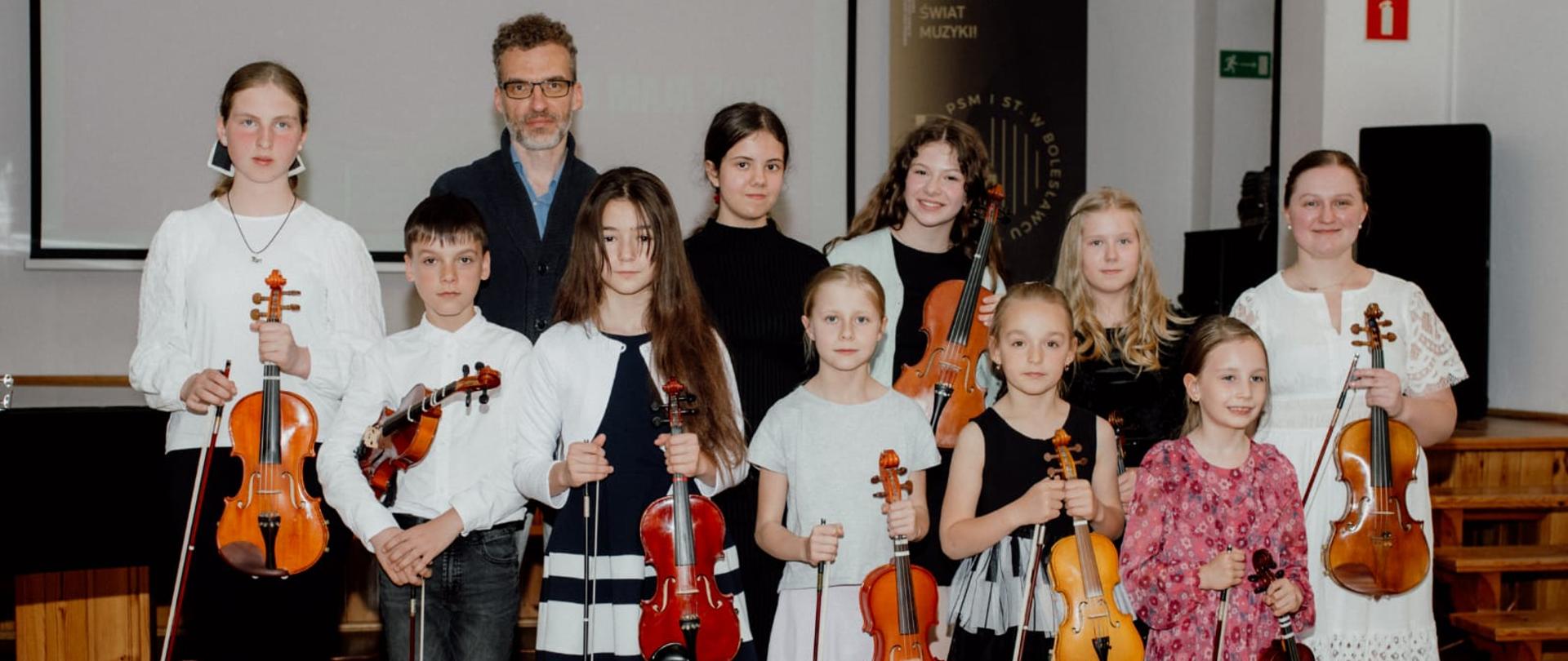 Zdjęcie przedstawiające wykonawców popisu klasy skrzypiec mgr Kingi Biesiadeckiej, który odbył się 20 maja 2025 roku w auli szkoły.