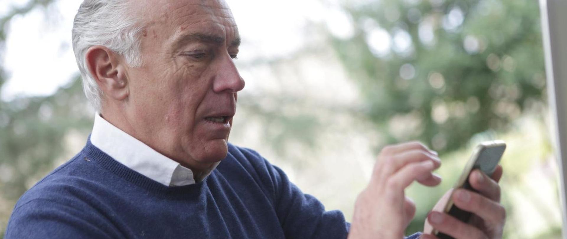 starszy pan naciska przyciski w telefonie