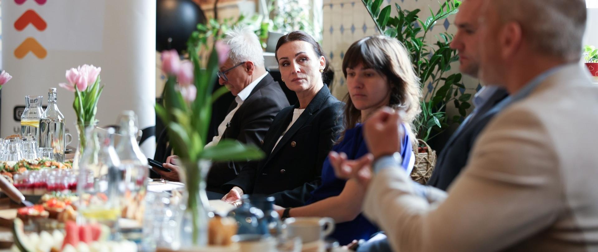 kilka osób siedzi przy stole i dyskutuje, w tle baner akcji „Alfabet NGO. Powiemy Ci coś, czego nie wiesz” 