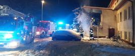 Po prawej stronie zdjęcia budynek DPS, po lewej stronie trzy pojazdy straży pożarnej z włączonymi sygnałami świetlnymi.