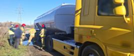 
Na pierwszym planie: ciągnik siodłowy z podpiętą naczepą typu cysterna ADR. W tle: funkcjonariusze Straży Pożarnej i Inspekcji Transportu Drogowego dokonują oględzin miejsca wycieku paliwa z cysterny.