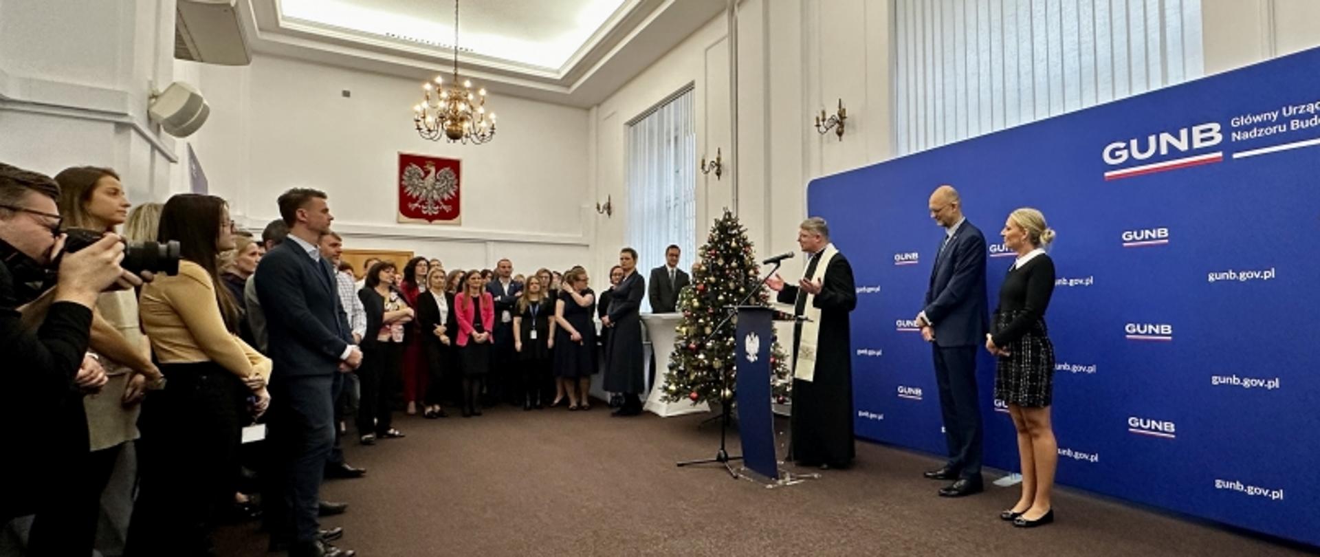 Wystąpienie podczas uroczystości w GUNB, w tle choinka, godło Polski i baner z logo GUN