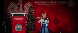 Występy artystyczne podczas uroczystości, dziewczynka gra na skrzypcach przy asyście opiekunki na scenie