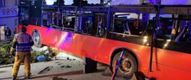 Zdjęcie przedstawia wypadek autobusu Miejskiego Zakładu Komunikacyjnego - autobus wjechał na murek o wysokości jeden metr taranując zaparkowany samochód osobowy. Na zdjęciu widoczne są działające służby - straż pożarna, policja, pogotowie ratunkowe oraz pracownicy Miejskiego Zakładu Komunikacyjnego.