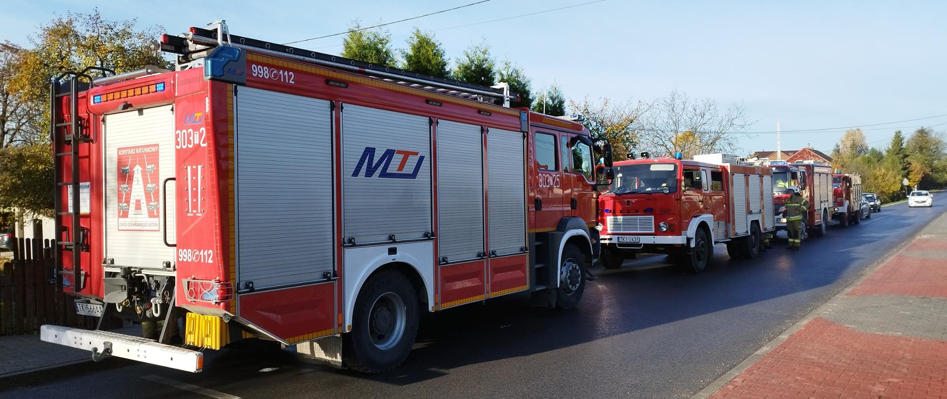 Zdjęcie przedstawia ulicę, na której stoi sznur samochodów pożarniczych biorących udział w akcji ratowniczej. 