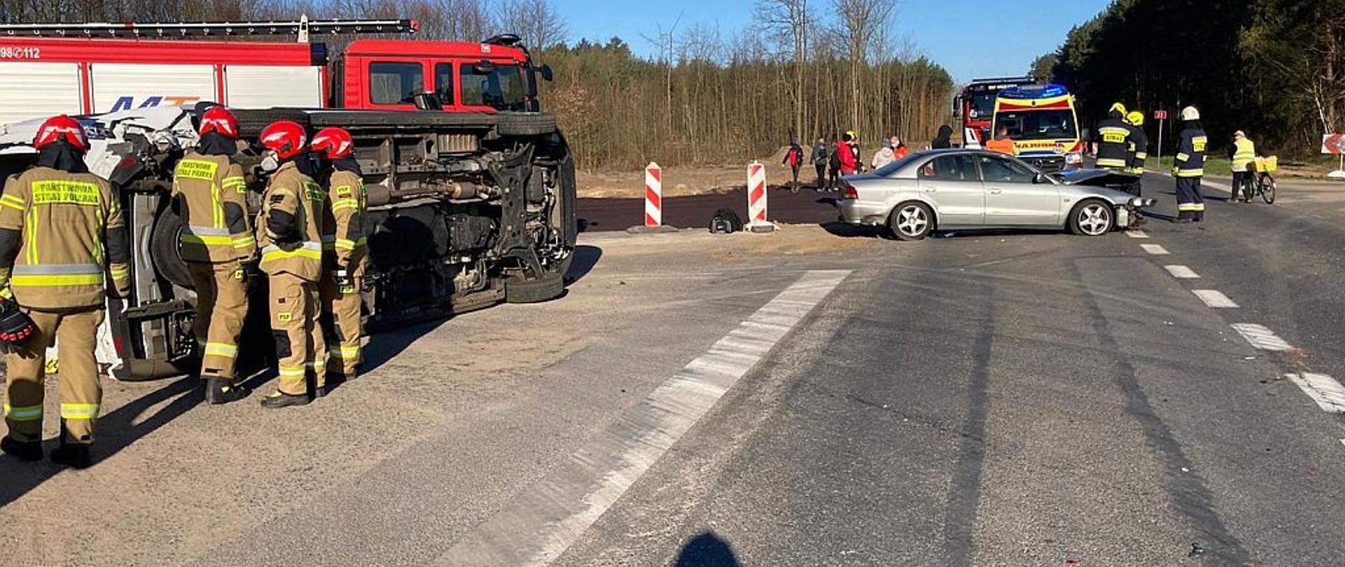 Na zdjęciu znajdują się w oddali dwa samochody oraz strażacy.