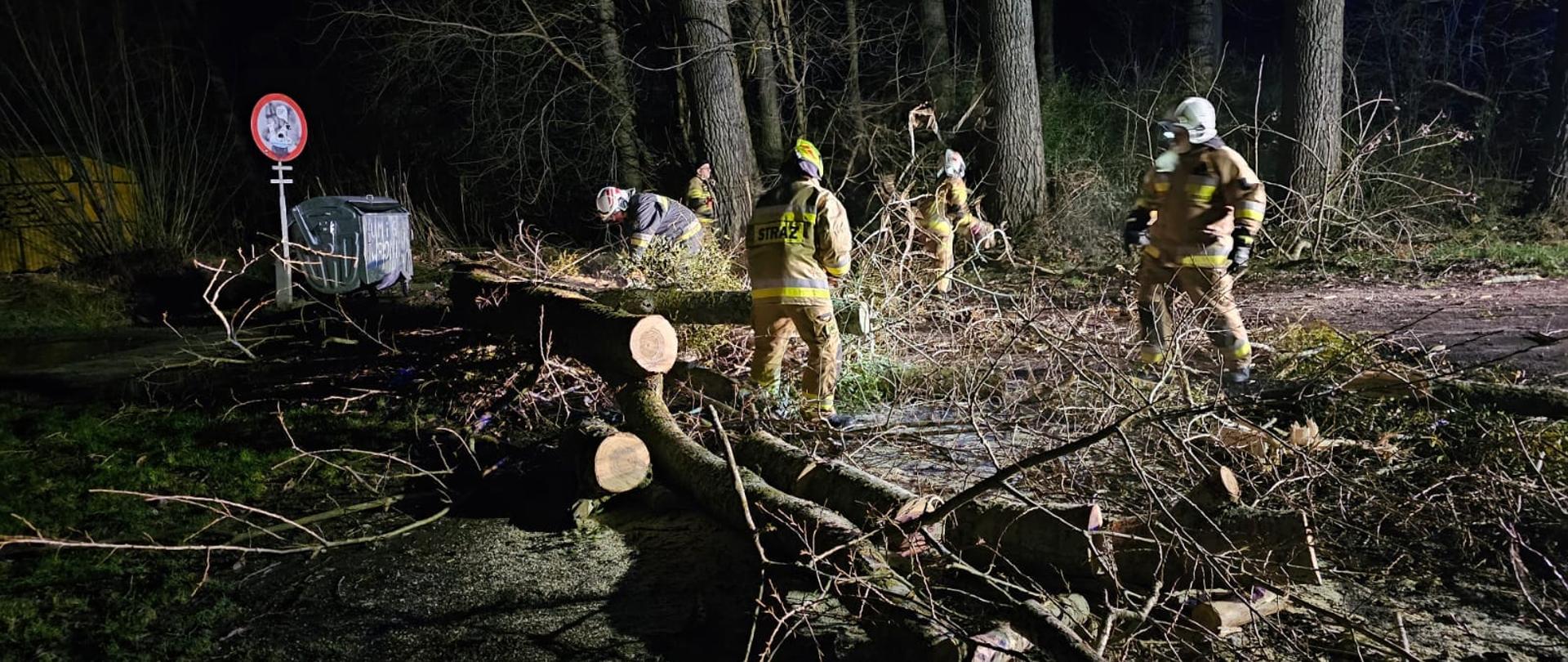 Strażacy usuwają drzewo z drogi, jest ciemno