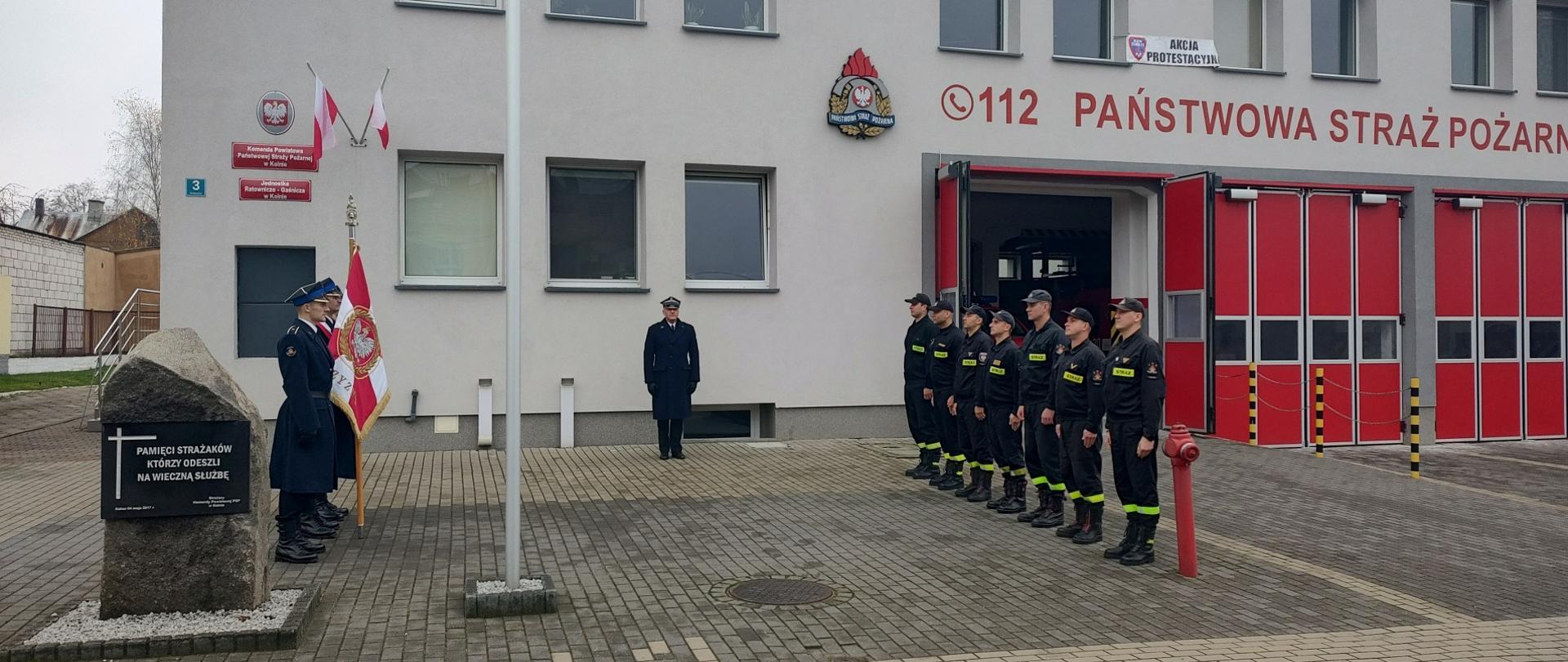 Na zdjęciu widać zmianę służbową, Komendanta i poczet flagowy przed strażnicą, przy maszcie z flagą śpiewających hymn Polski