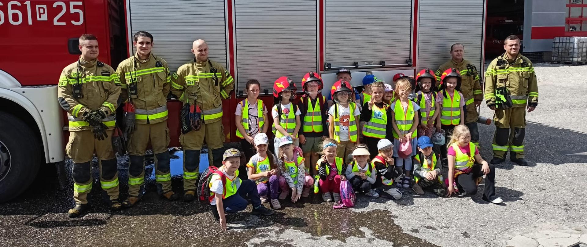 Wspólne zdjęcie strażaków z dziećmi na tle samochodu pożarniczego.