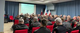 odprawa pionu kontrolno-rozpoznawczego PSP województwa mazowieckiego. uczestnicy siedzą na krzesłach w sali konferencyjnej. na przodzie przy mównicy siedzi zastępca mazowieckiego komendanta PSP oraz naczelnicy wydziału kontrolno-rozpoznawczego komendy wojewódzkiej psp w warszawie. w tle wyświetlana jest prezentacja na rzutniku.