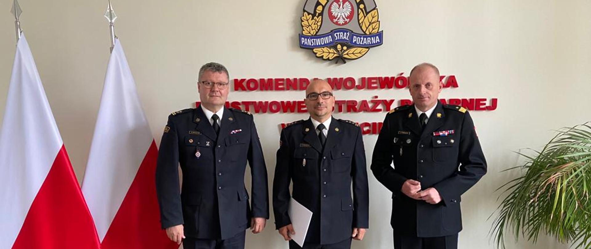 Wręczenie nagrody z okazji 30-lecia służby dla st.bryg. Piotra Juzyszyna przez nadbryg. Jarosława Tomczyka, w tle flagi Polski, kwiat i logo PSP.
Od lewej Komendant Powiatowy PSP w Gryfinie bryg. Sławomir Michalski, po prawej nadbryg. Jarosław Tomczyk, w środku st.bryg. Piotr Juzyszyn