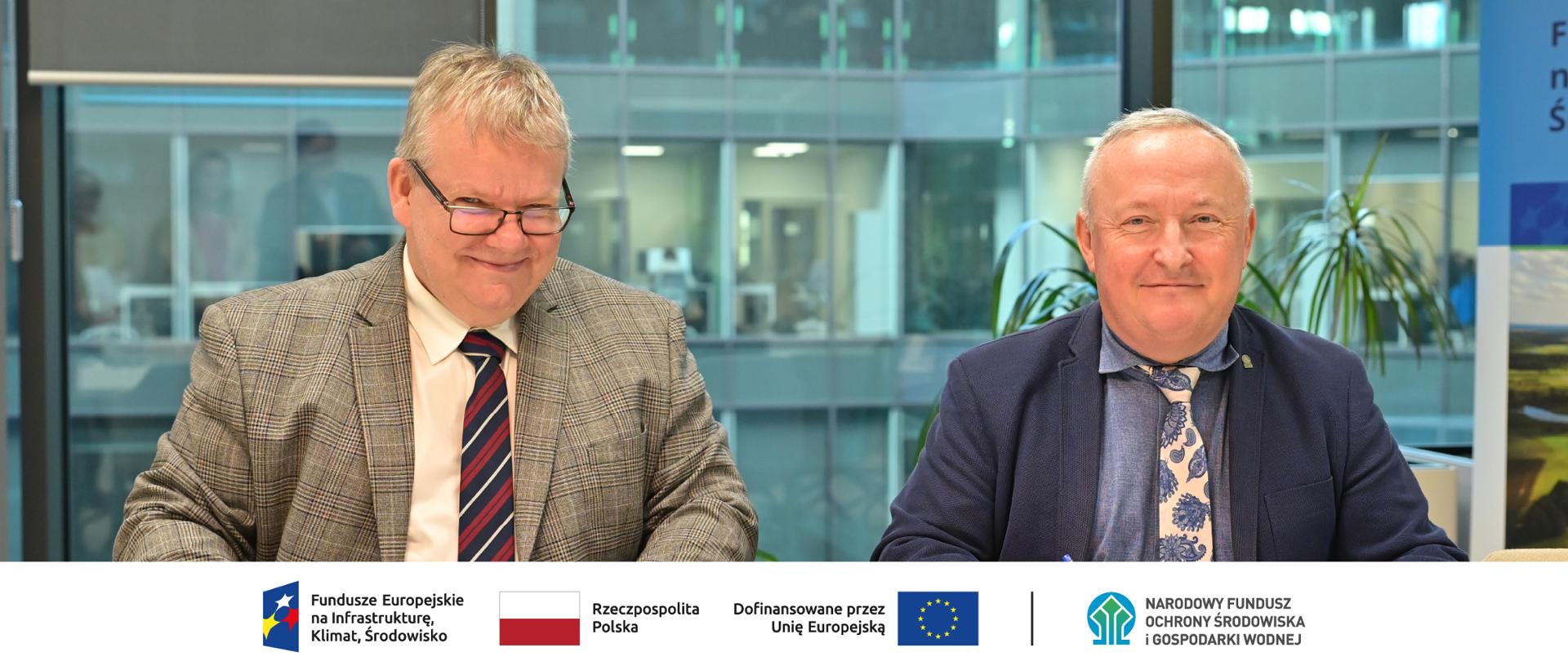 Podpisanie umowy w siedzibie NFOŚiGW. Na zdjęciu od lewej Adam Ciekański, prezes zarządu Centrum Zielonej Energii i Paweł Augustyn, zastępca prezesa zarządu NFOŚiGW. W stopce planszy ciąg logotypów: Fundusze Europejskie na Infrastrukturę, Klimat, Środowisko, flaga Rzeczypospolita Polska, flaga UE Dofinansowane przez Unię Europejską, logo NFOŚiGW.
