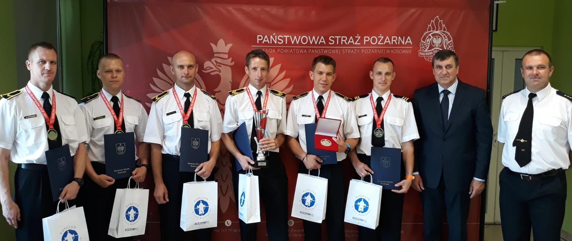 SPOTKANIE STRAŻAKÓW Z BURMISTRZEM. Na zdjęciu funkcjonariusze stoją w rzędzie razem z burmistrzem do pamiątkowego zdjęcia. 