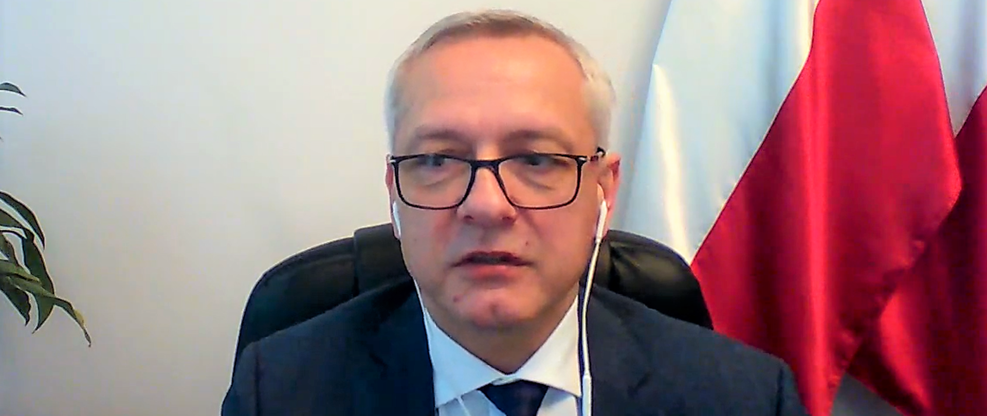 Marek Zagórski - minister cyfryzacji ze słuchawkami na uszach ze swojego gabinetu przemawia do uczestników wideokonferencji.