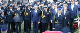 Strażacy oddają honor uczestnicy obchodów stoją na baczność przed trumnami przykrytymi flagą Polski.