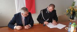 Zdjęcie przedstawia druha Krzysztofa Czapkę, prezesa Ochotniczej Straży Pożarnej w Kraczkowej, który w towarzystwie Posła na Sejm Kazimierza Gołojucha podpisuje umowę.