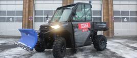 Na zdjęciu widzimy pojazd typu quad UTV Ranger 1000. Pojazd ma podpięty z przodu pług do odśnieżania. Pojazd stoi przed budynkiem Komendy Powiatowej Państwowej Straży Pożarnej w Lesku. 