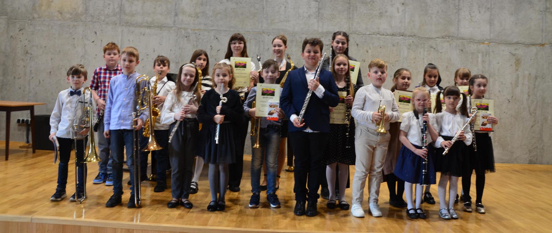 Uczniowie na scenie sali koncertowej w rękach trzymają instrumenty dęte