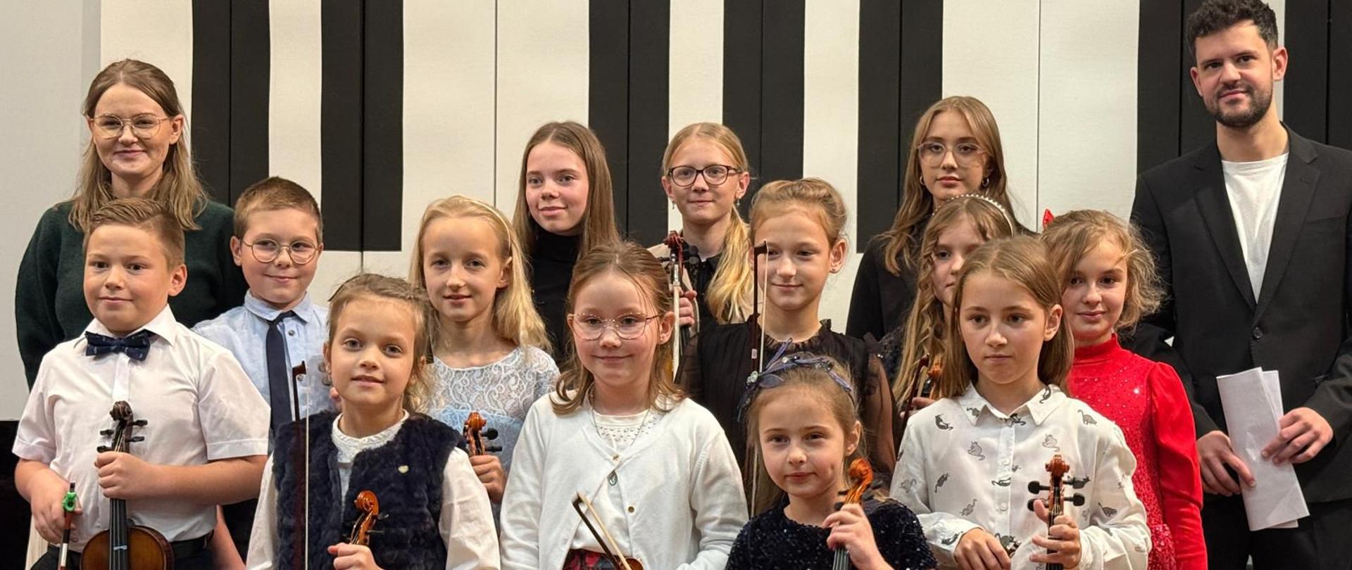 Wszyscy wykonawcy razem z nauczycielką stoją na scenie.