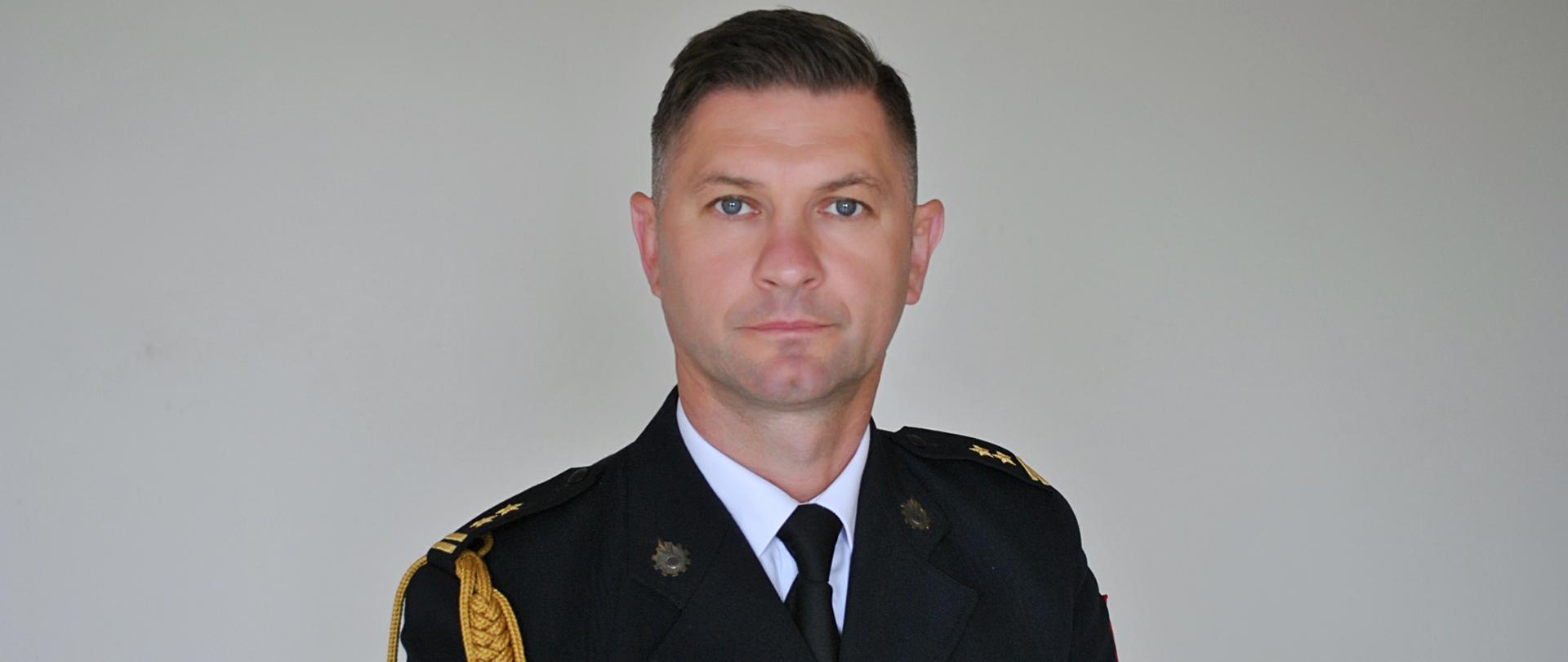 Komendant Powiatowy PSP w mundurze koloru grafitowego ze sznurem na szarym tle