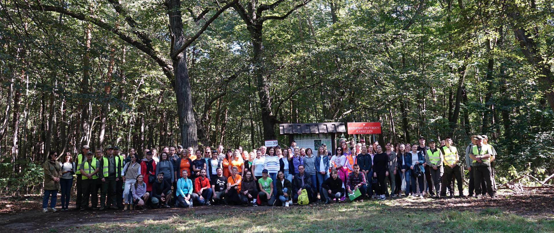 Zdjęcie grupowe - uczestnicy akcji sprzątania na tle lasu i tablic informacyjnych 
