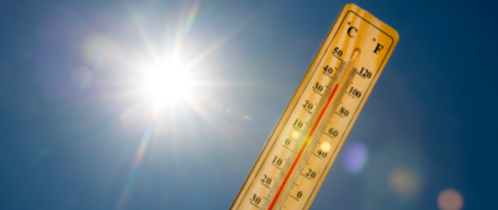 Termometr wskazujący wysoką temperaturę na tle bezchmurnego nieba i świecącego słońca.