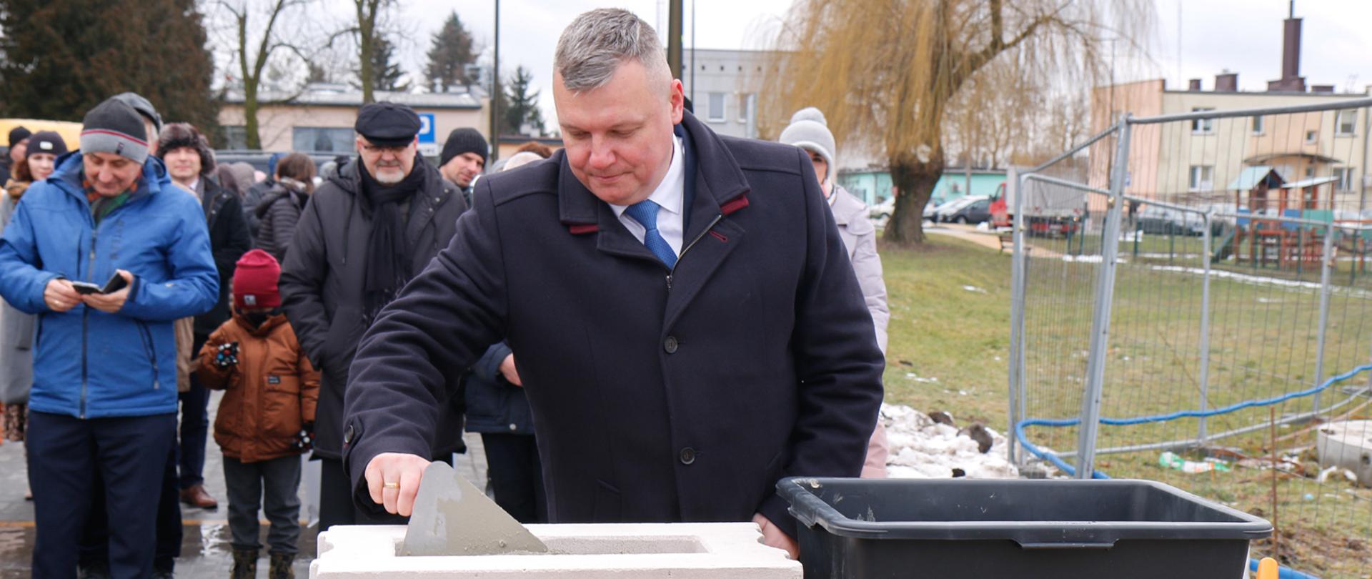 Wicewojewoda Robert Gmitruczuk wmurowuje kamień węgielny, w tle uczestnicy uroczystości.
