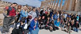 Na zdjęciu widzimy grupę uczniów i nauczycieli biorących udział artystycznej wyprawie do Grecji. Fotografia autorstwa Katarzyny Gwizdała-Kłak została wykonana na wzgórzu Akropolu. W tle widzimy świątynię Partenon.