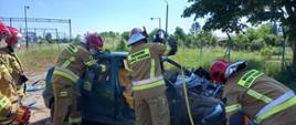 Strażacy rozcinają samochód osobowy za pomocą narzędzi hydraulicznych, ćwiczą ewakuację poszkodowanego z wnętrza pojazdu.