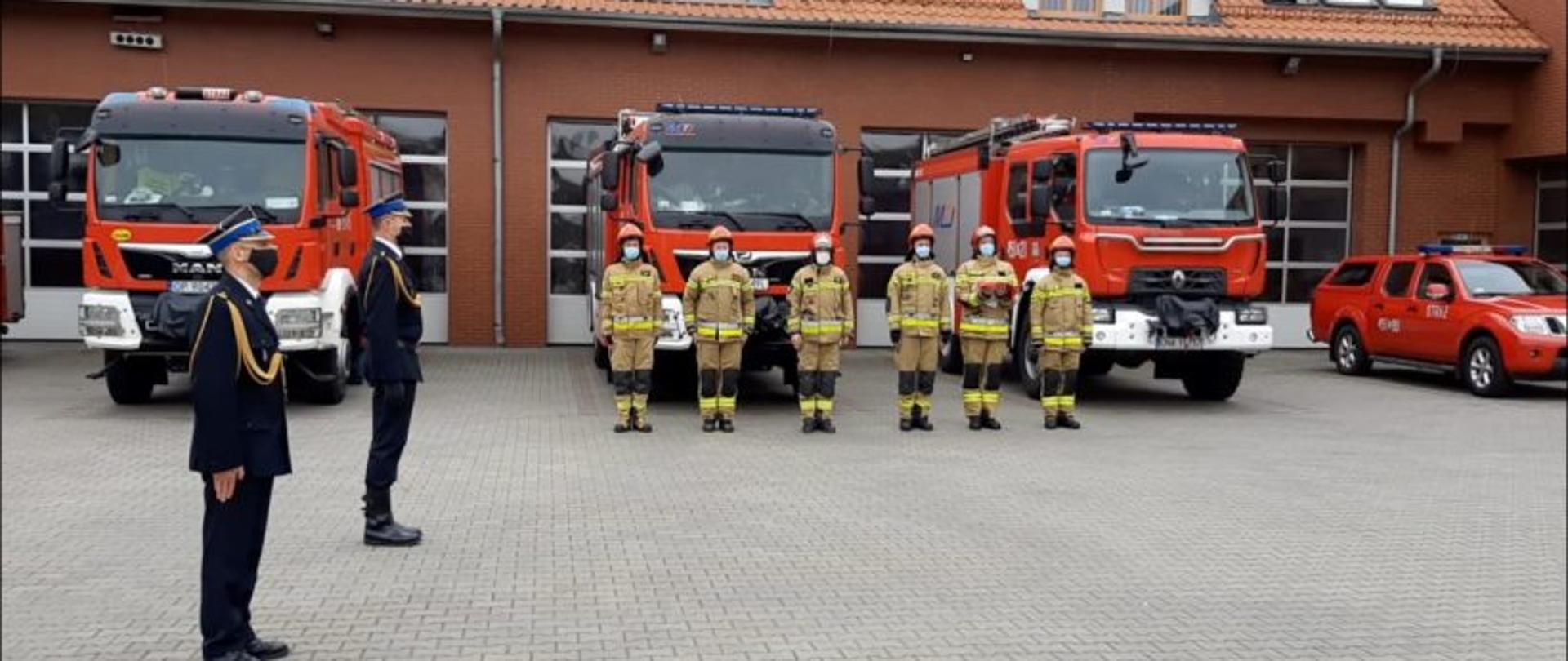 Pododdział strażaków Komendy Powiatowej PSP w Namysłowie na tle budynku komendy oraz samochodów ratowniczo-gaśniczych.