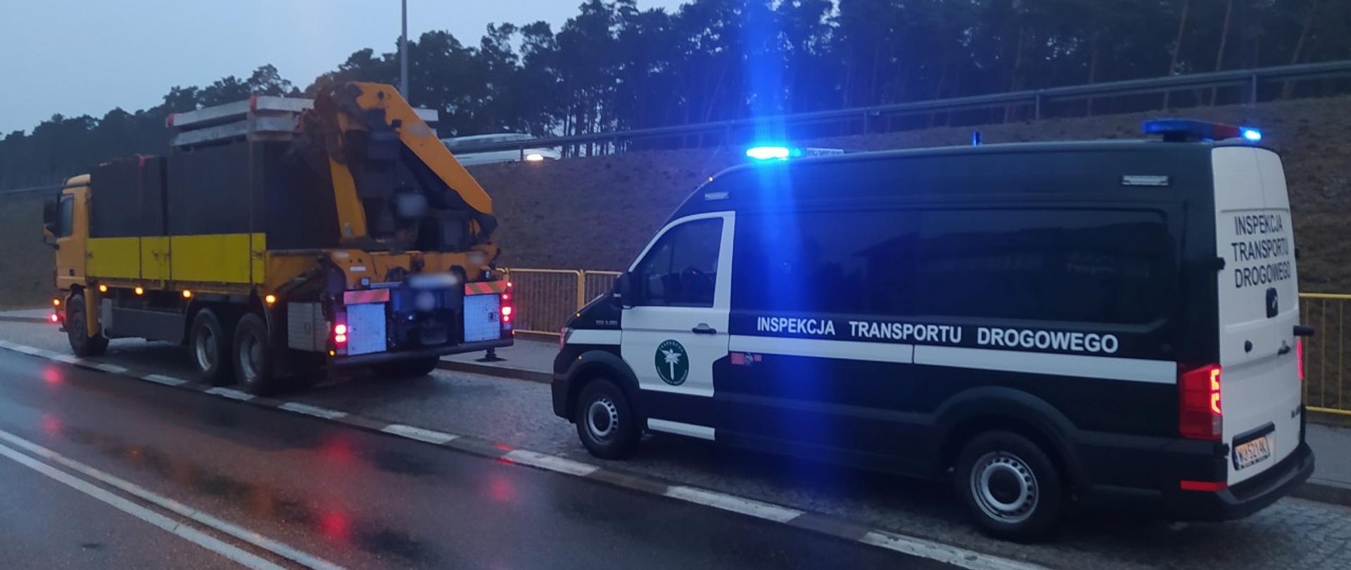 Ciężarówka z szambami betonowymi zatrzymana do kontroli drogowej i stojący za nią radiowóz ITD z włączoną sygnalizacją świetlną uprzywilejowania.