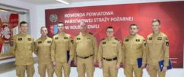 Na zdjęciu widzimy wszystkich mianowanych w towarzystwie Komendanta Powiatowego i jego zastępcy. W tle na ścianie sztandar Komendy oraz napis na płótnie Komenda Powiatowa Państwowej Straży Pożarnej w Kolbuszowej wraz z logotypem PSP i herbem Kolbuszowej