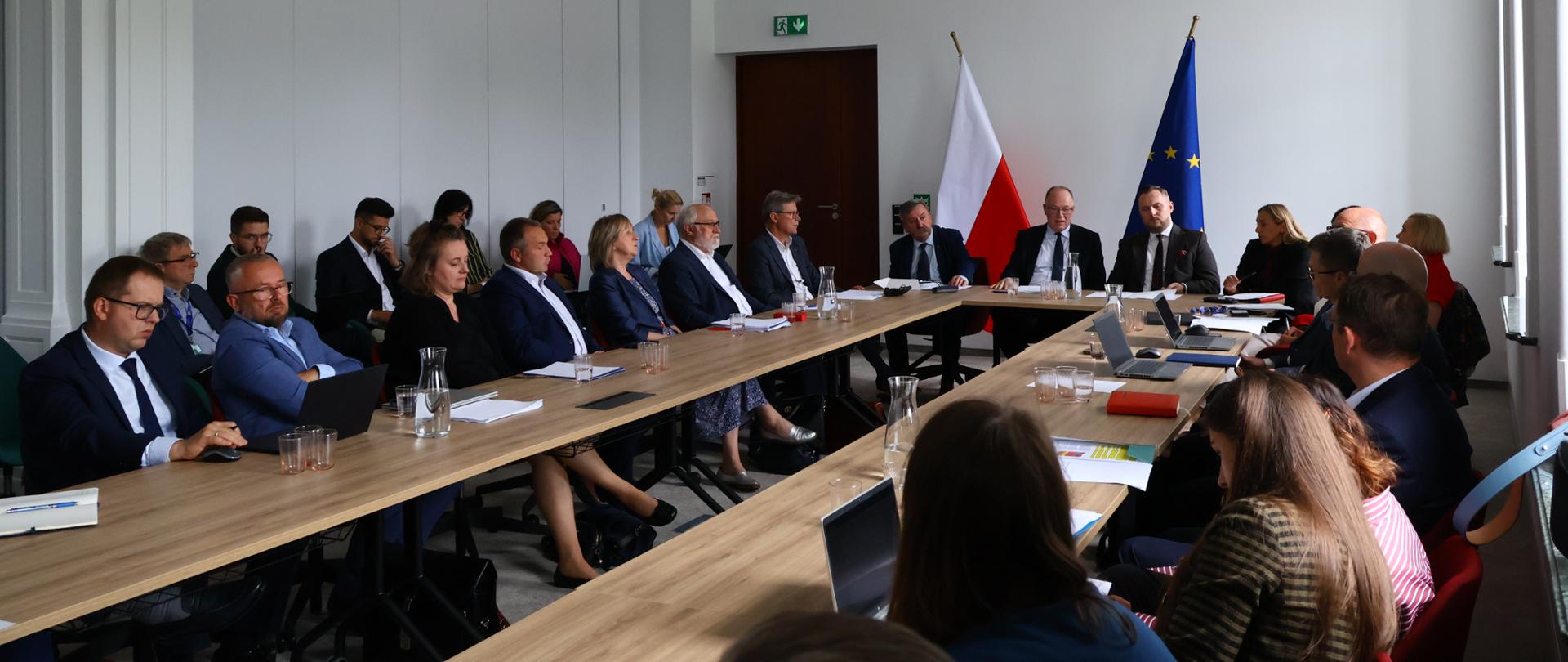 Spotkanie w Ministerstwie Energii z udziałem przedstawicieli administracji rządowej, regulatora i branży. Przy stole konferencyjnym obradują m.in. Wiceminister Energii Konrad Wojnarowski oraz Wiceminister Klimatu i Środowiska, Główny Geolog Kraju Krzysztof Galos. W tle widoczne są flagi Polski i Unii Europejskiej.