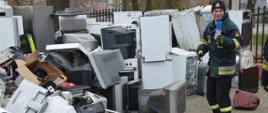 Strażacy dla Tosi. Plac komendy w Rawiczu. Na nim złożone są elektrośmieci w postaci m.in lodówek, monitorów komputerowych, drukarek, itp. Obok stoi strażak, trzymając w ręce plastikową butelkę do mleka.