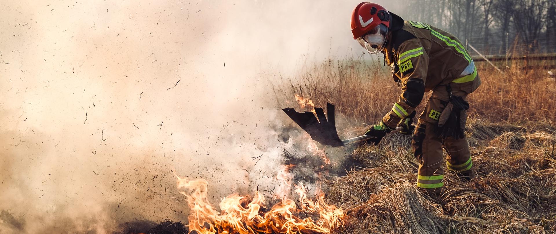 Strażak przy użyciu tłumicy gasi pożar trawy tłumicą