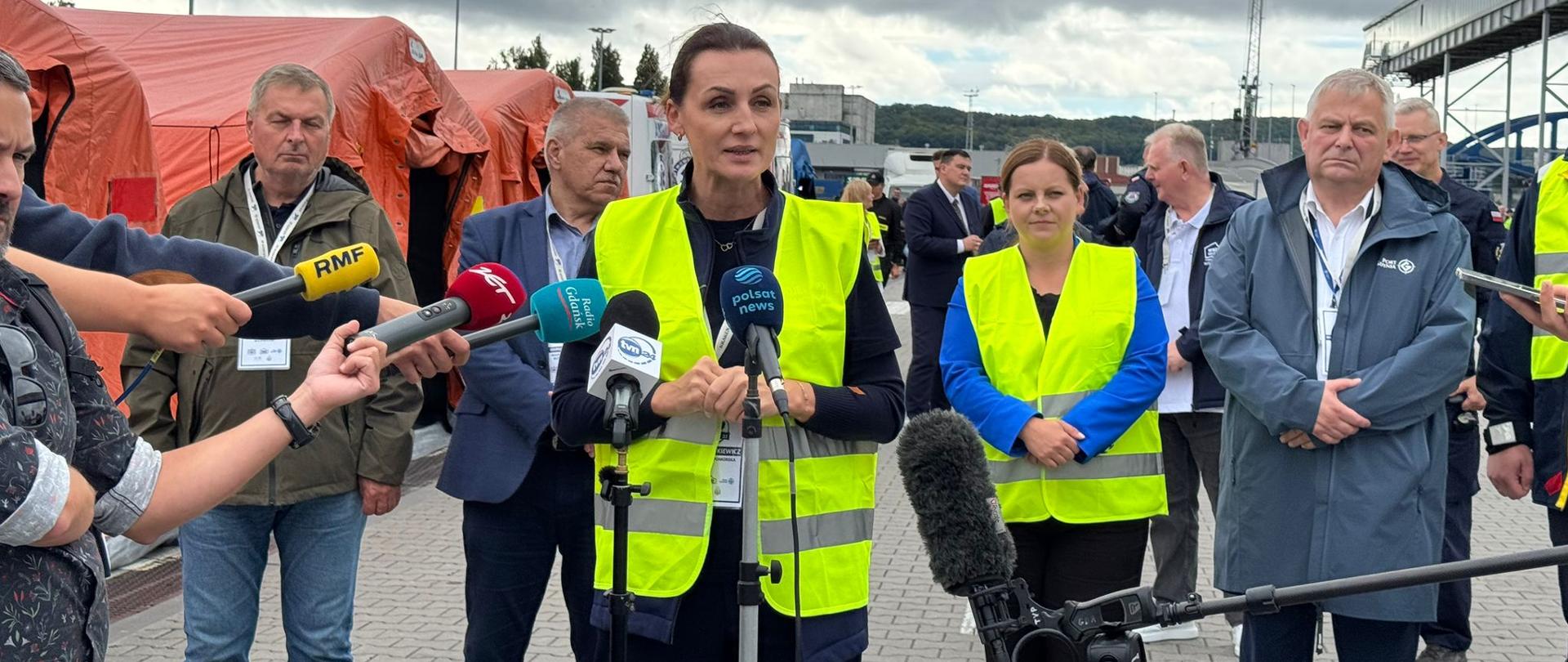 kobieta w żółtej odblaskowej kamizelce stoi przed mikrofonem podczas konferencji prasowej