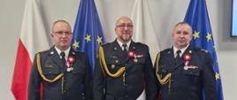 Na zdjęciu znajdują się Komendant Powiatowy PSP bryg. Wojciech Wanat, Zastępca Komendanta PSP st. kpt. Krzysztof Minga oraz funkcjonariusz st. ogn. Zbigniew Labuhn. Wszyscy ubrani są w mundury galowe, a na prawym ramieniu mają założone sznury galowe. 