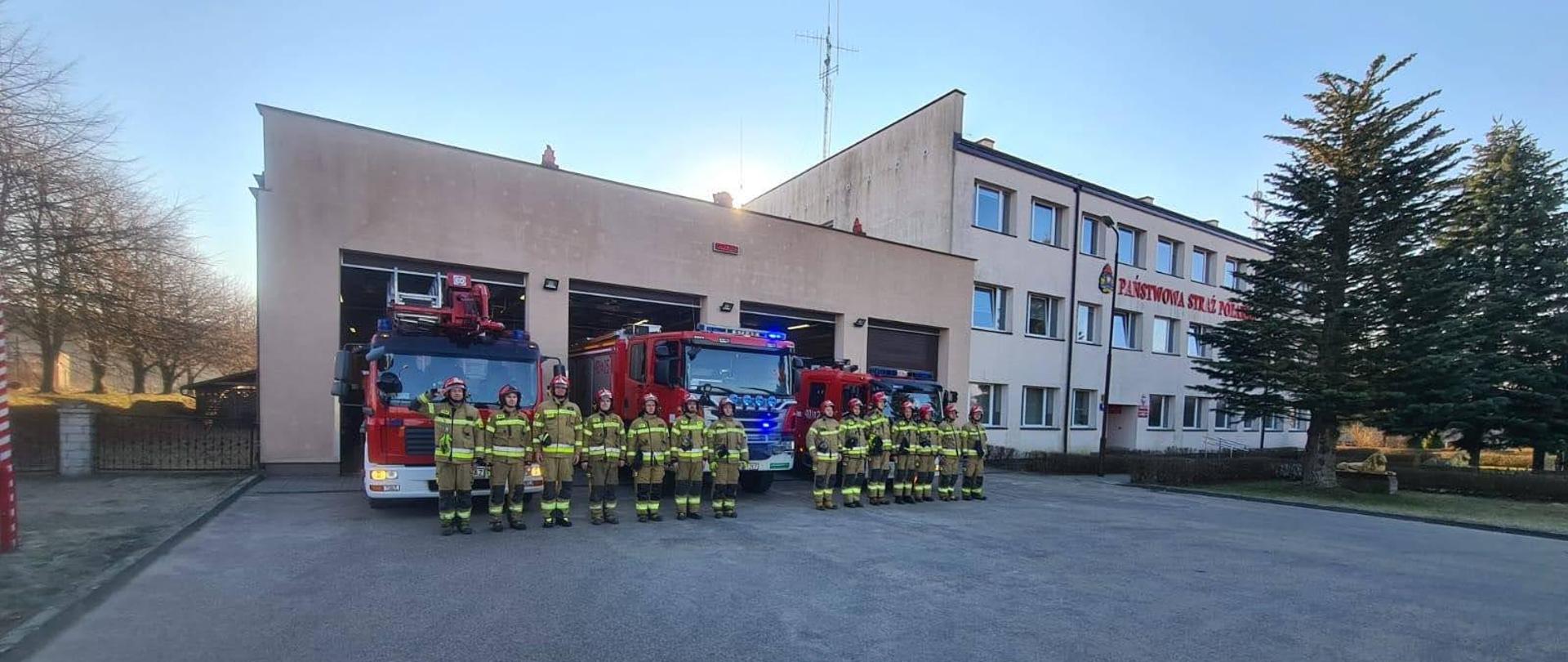 Strażacy stojąc na baczność na tle samochodów gaśniczych oddają cześć poległym strażakom z Ukrainy.