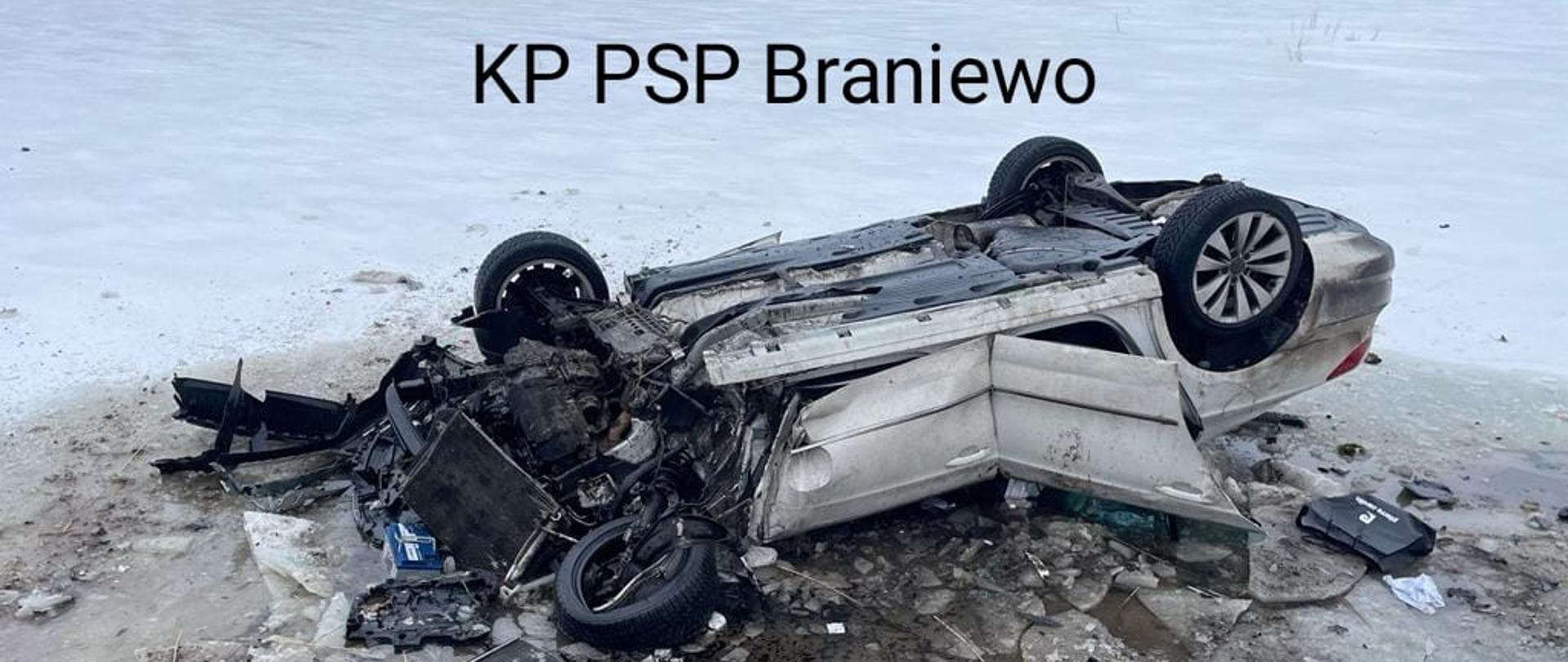 Samochód osobowy leży na dachu, mocno rozbity. Wokół białe pole od śniegu.